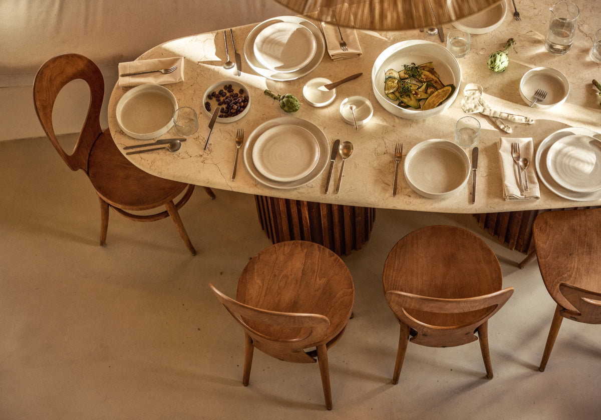 Gedeckter Esstisch mit beigen Tellern und Designer-Holzstühlen von oben fotografiert